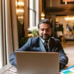 Elegant businessman in office setting working on laptop, showcasing success and professionalism.