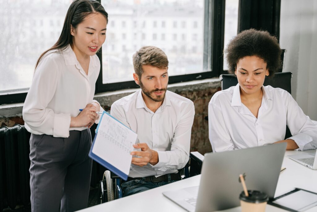 A diverse team working together on a laptop in a modern office setting, promoting inclusivity and collaboration.